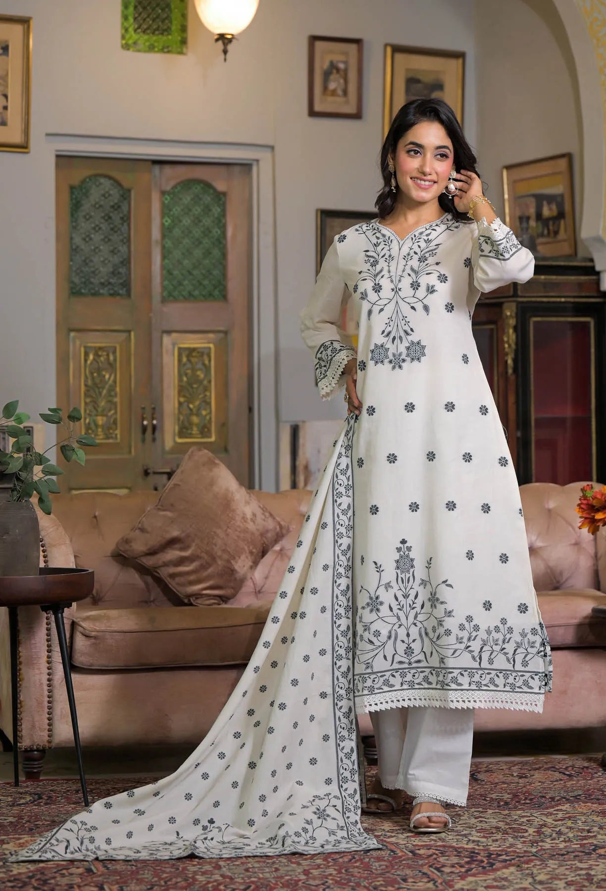 Woman in a white embroidered outfit standing in a living room.