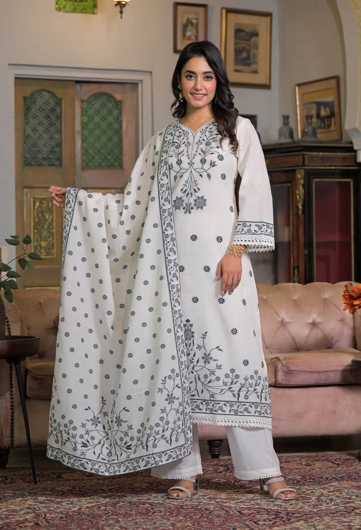 Woman in a white embroidered traditional outfit standing in a decorated room.