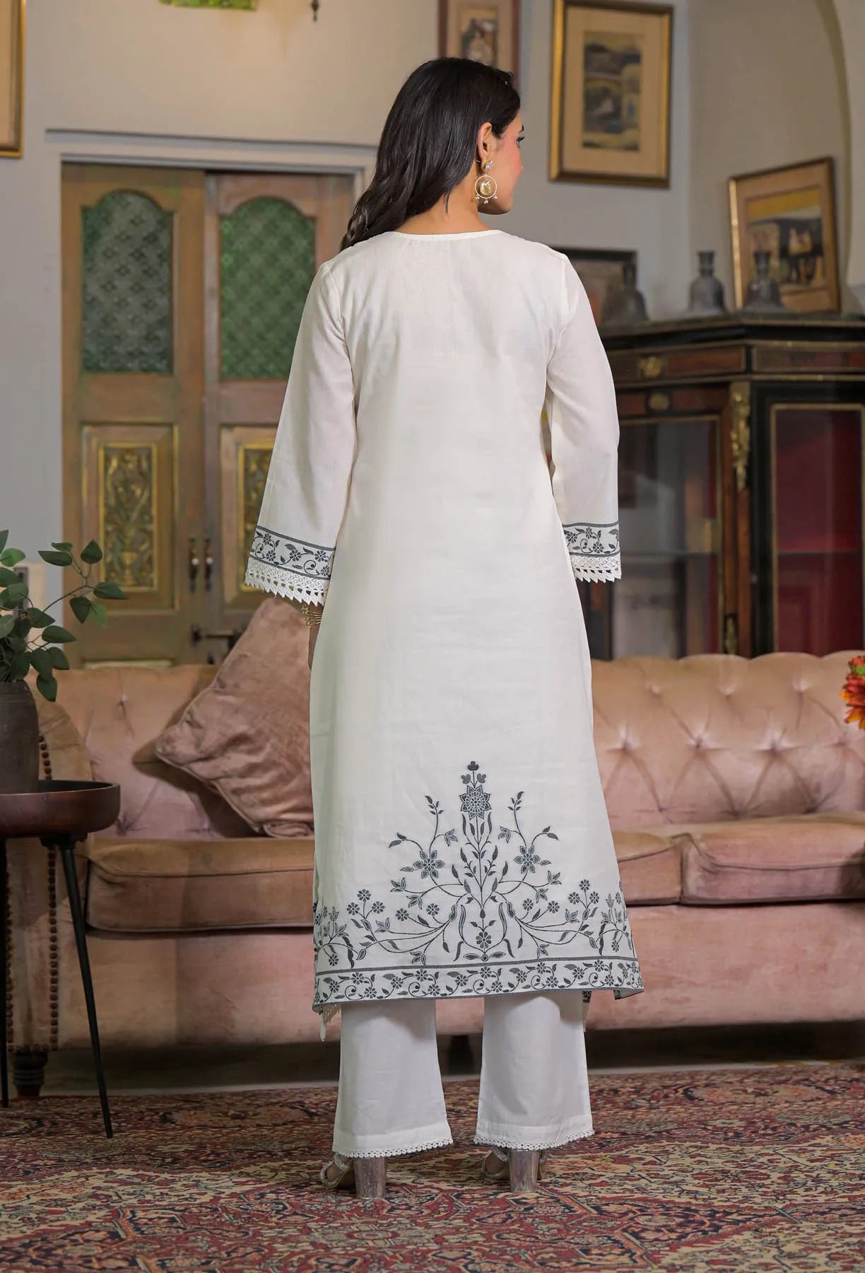 Woman wearing a light-colored embroidered kurta in a living room setting.