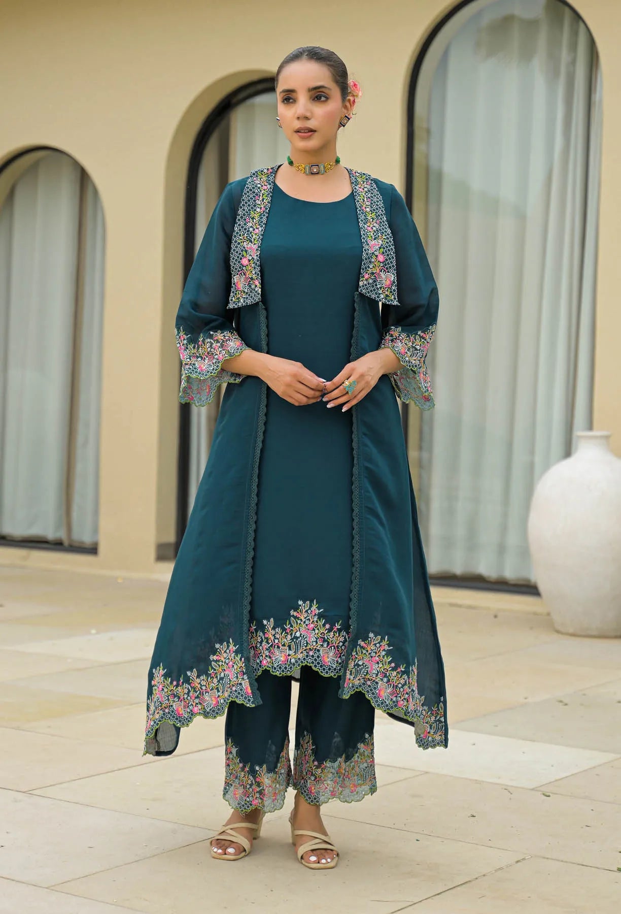 Woman wearing a teal outfit with floral embroidery standing outdoors.