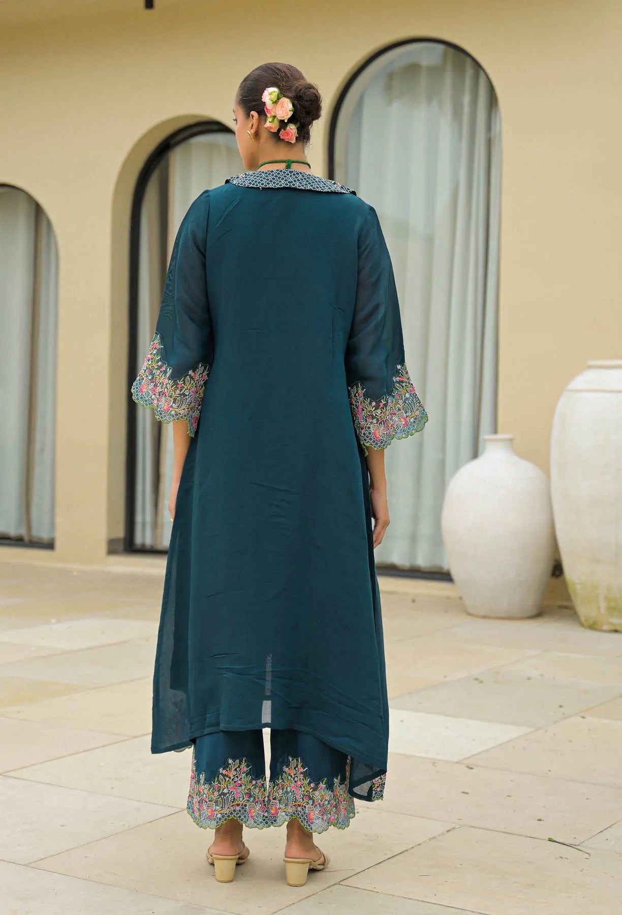 Woman wearing a teal traditional outfit with floral embroidery in an outdoor setting.