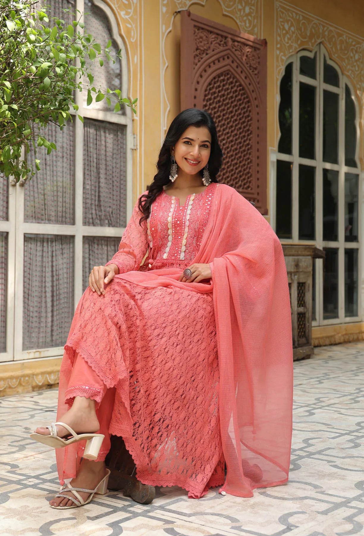Woman in a pink traditional outfit sitting outdoors with decorative architecture in the background