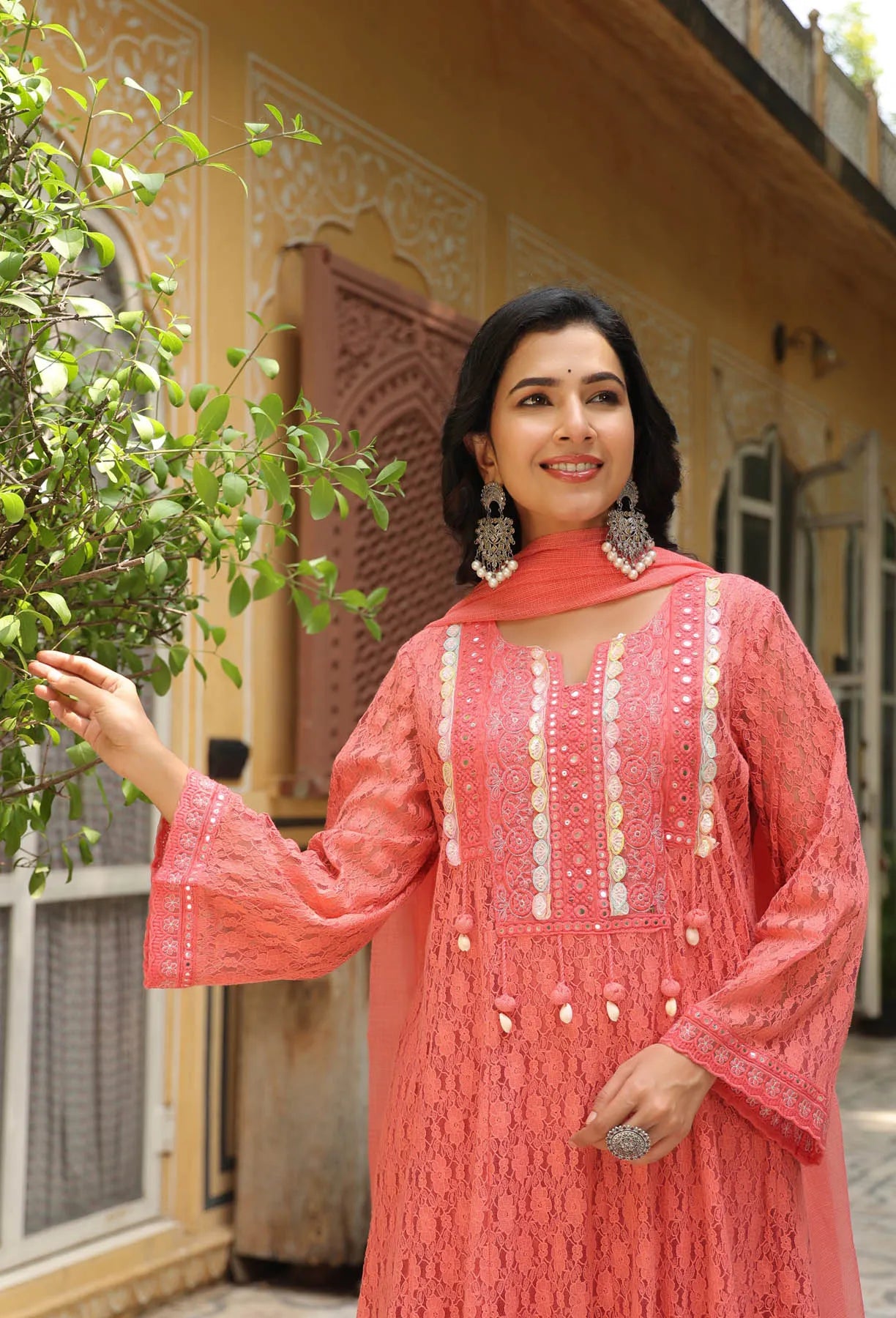 Woman in a pink traditional outfit standing outdoors with a building in the background