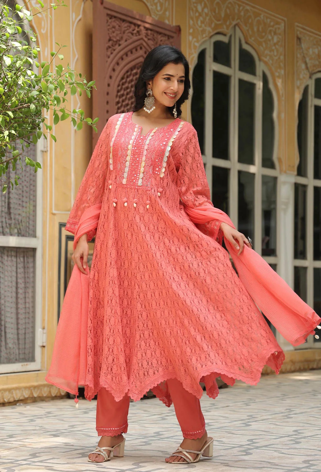 Woman wearing a pink traditional outfit with intricate designs in an outdoor setting.