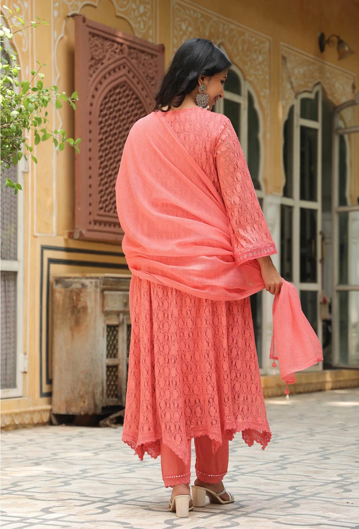 Woman in a coral pink traditional outfit standing in front of a decorative building.