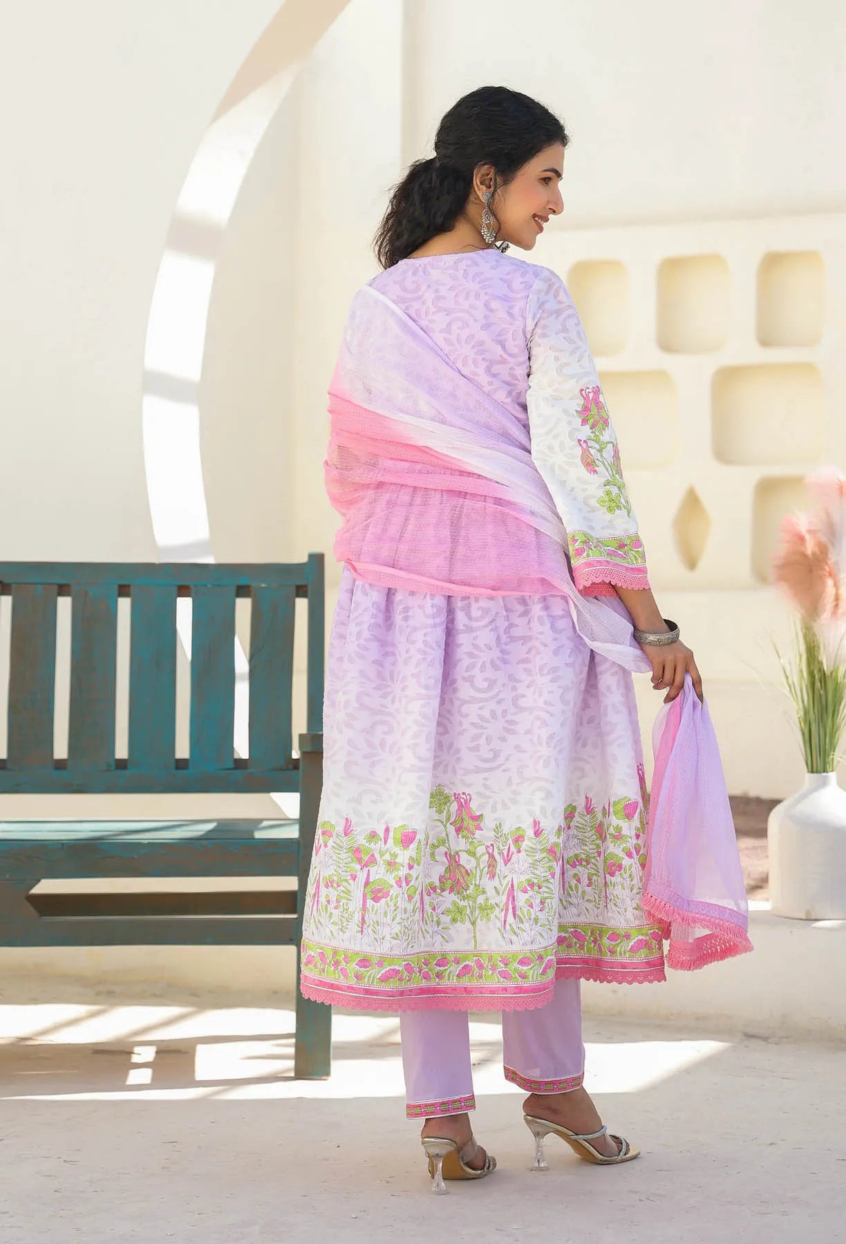 Woman wearing a light purple and pink traditional outfit with floral patterns in a bright room.