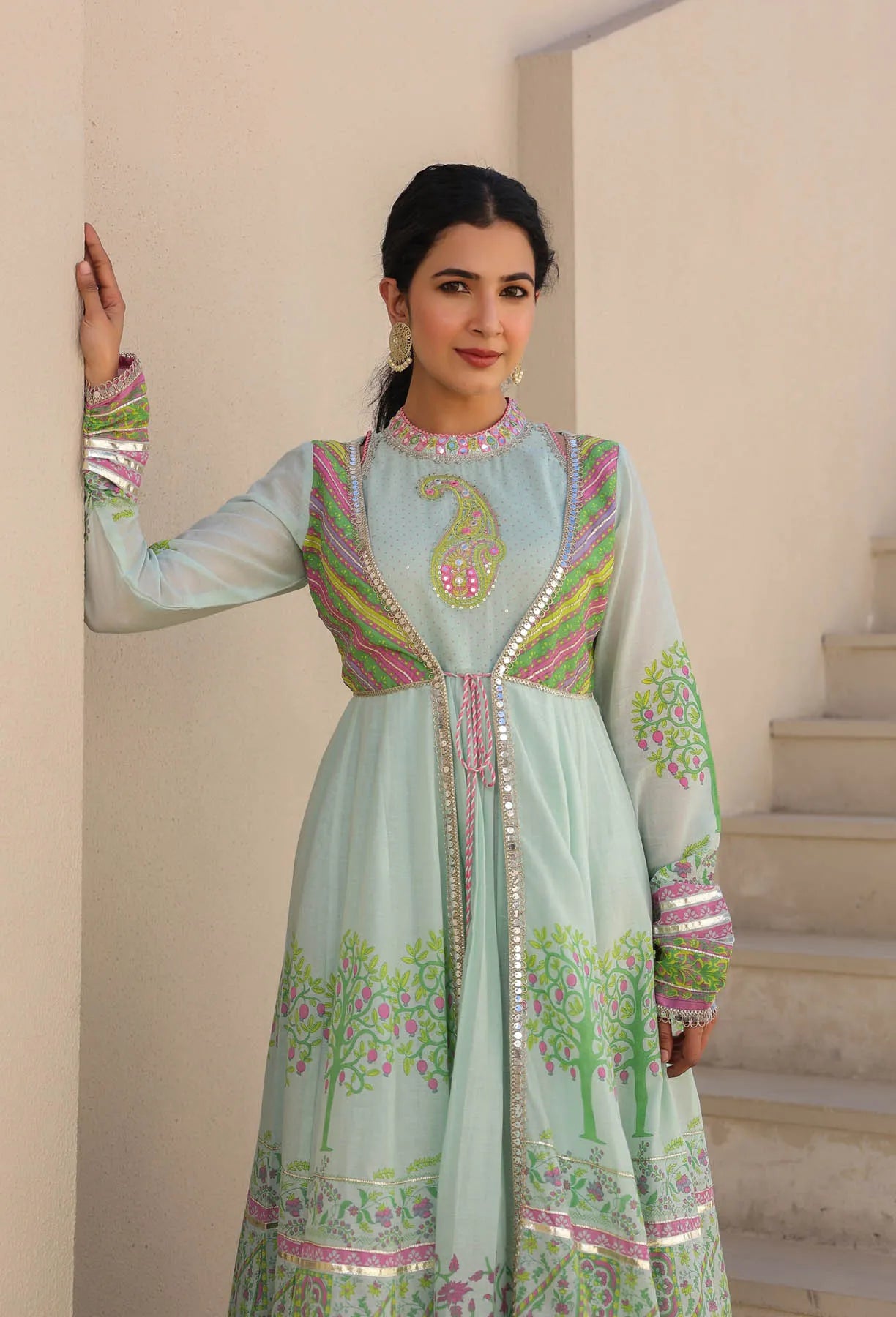 Woman wearing a light blue embroidered traditional outfit in a neutral setting