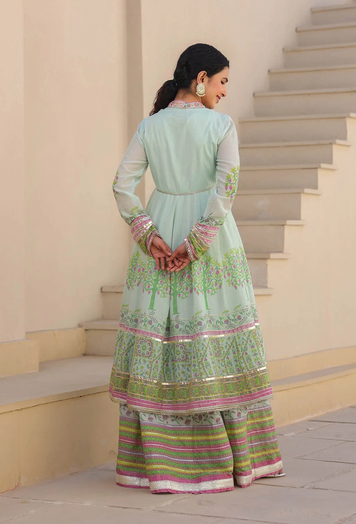 Woman in a light blue traditional outfit with floral patterns standing on steps.