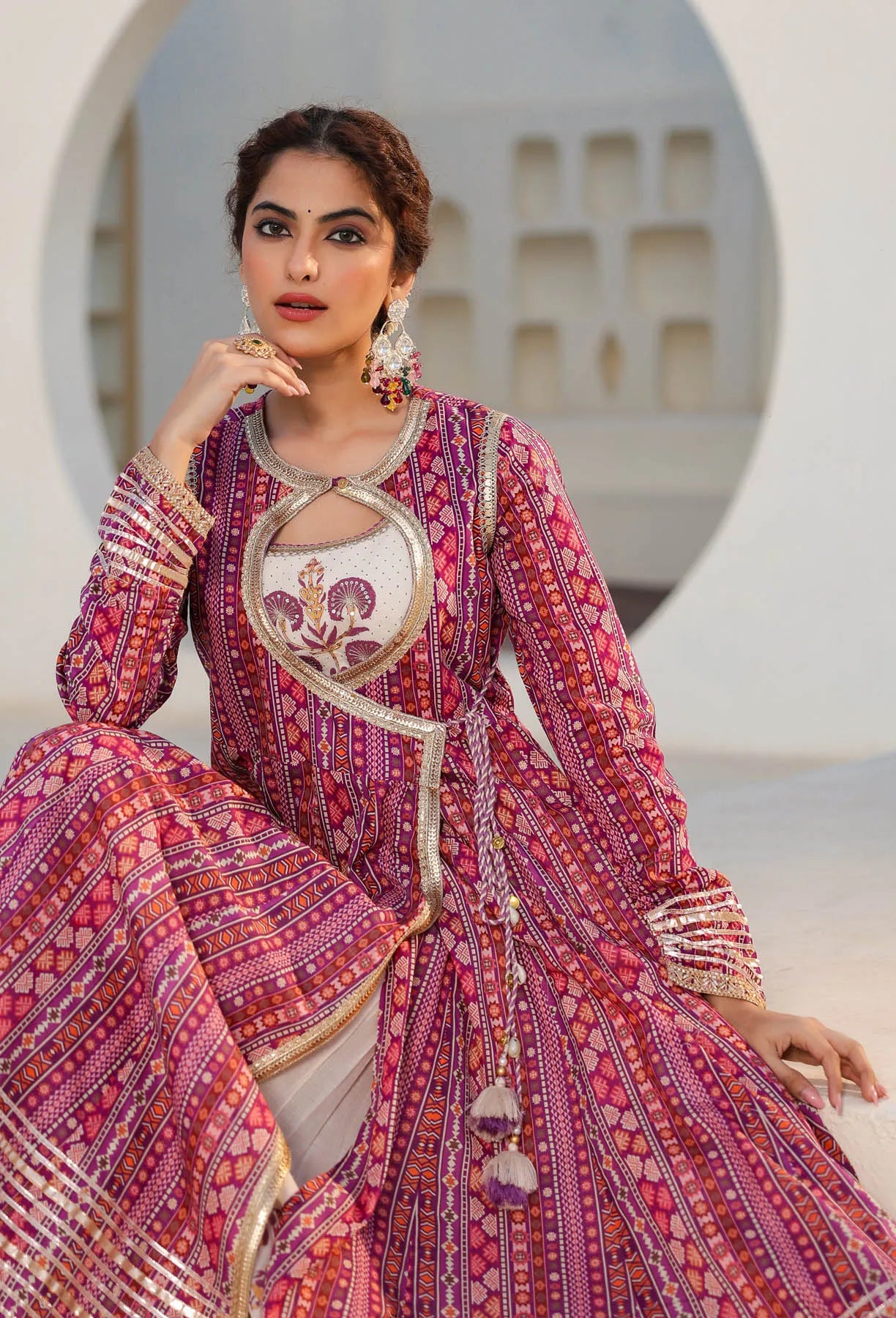 Woman wearing a traditional pink and red embroidered outfit with intricate patterns.