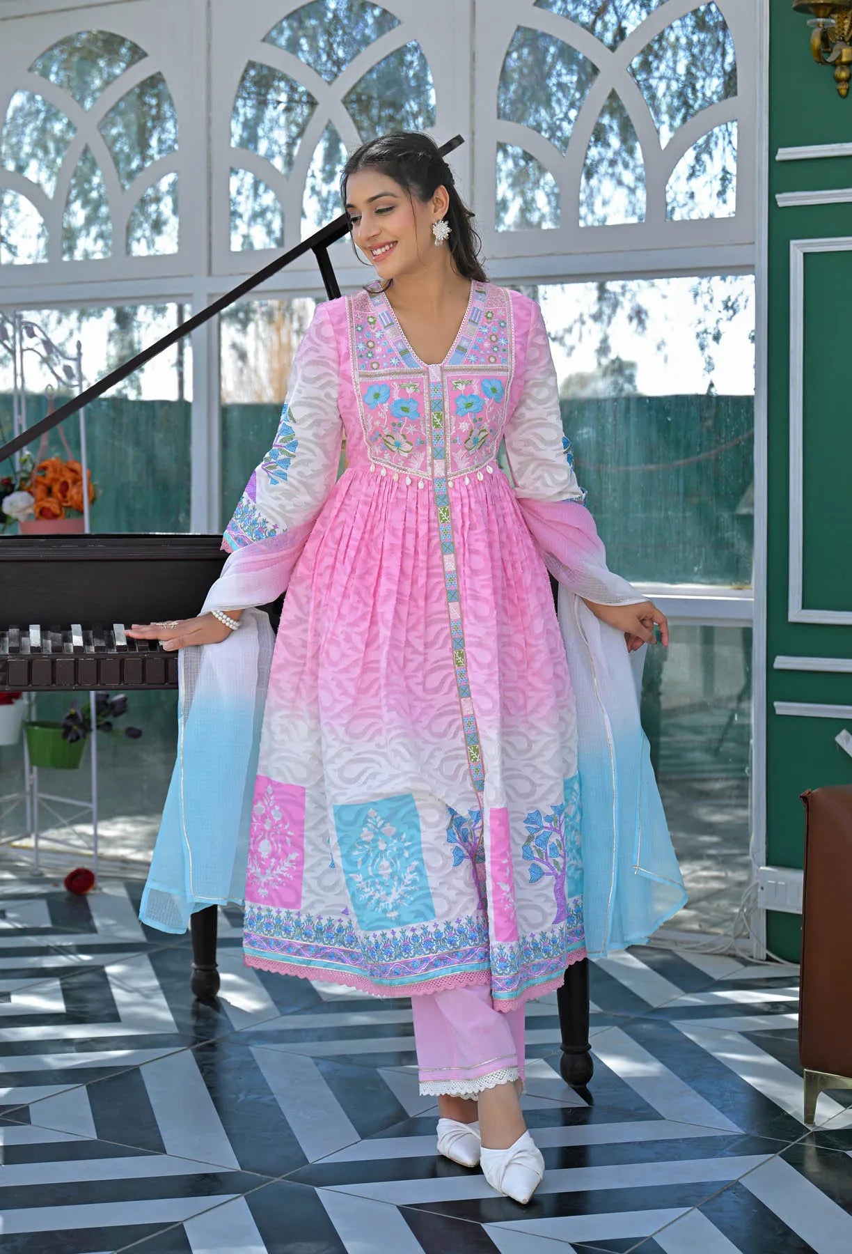 Woman in a pink and blue traditional outfit standing in a decorated room.