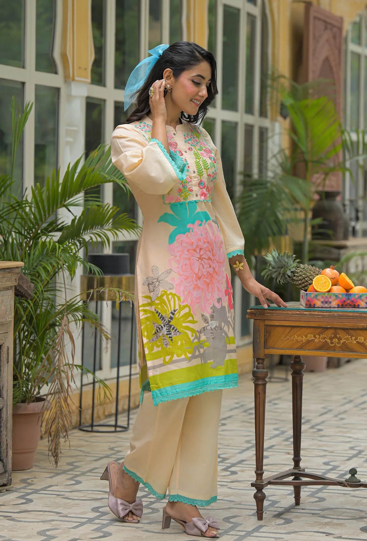 Woman in a floral dress standing in an outdoor setting with plants and a table.
