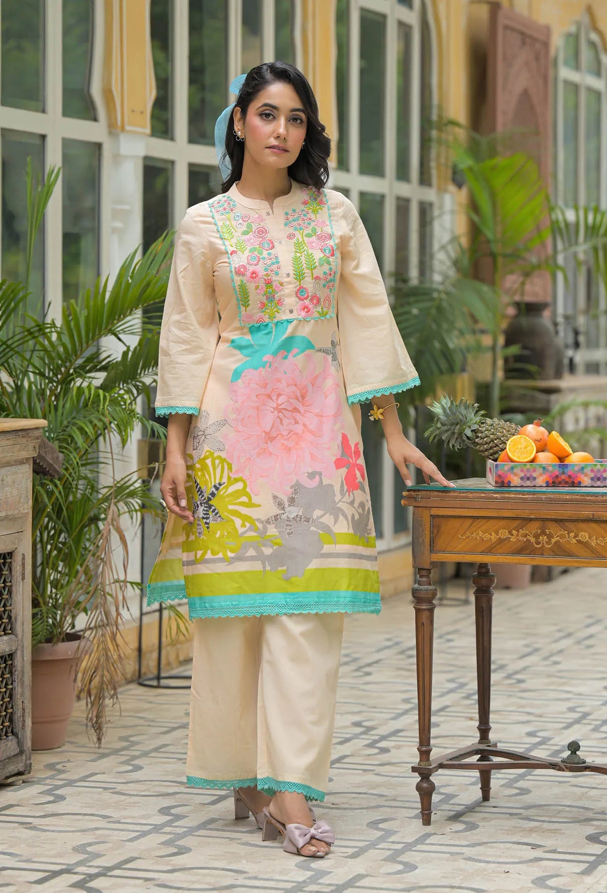 Woman in a floral dress standing in an outdoor setting with plants and a table.