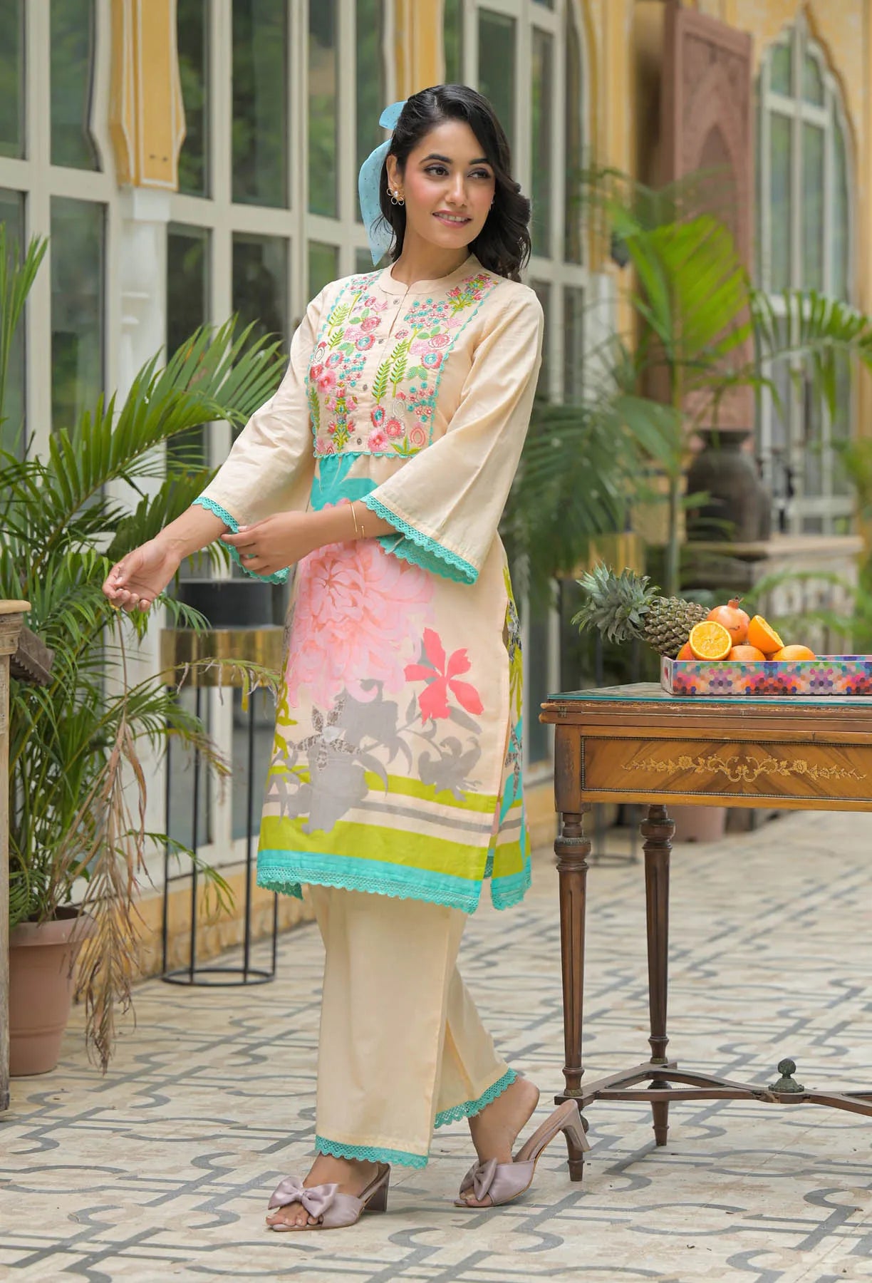 Woman in a floral outfit standing outdoors with plants and a table in the background