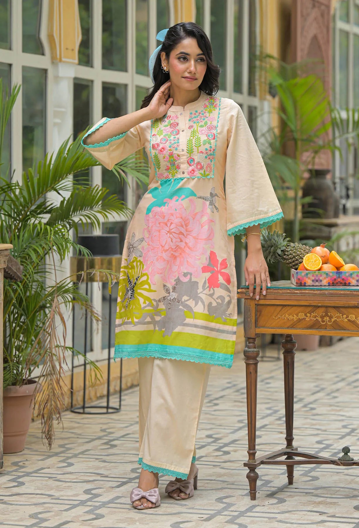 Woman in a floral dress standing in an outdoor setting with plants and a table.