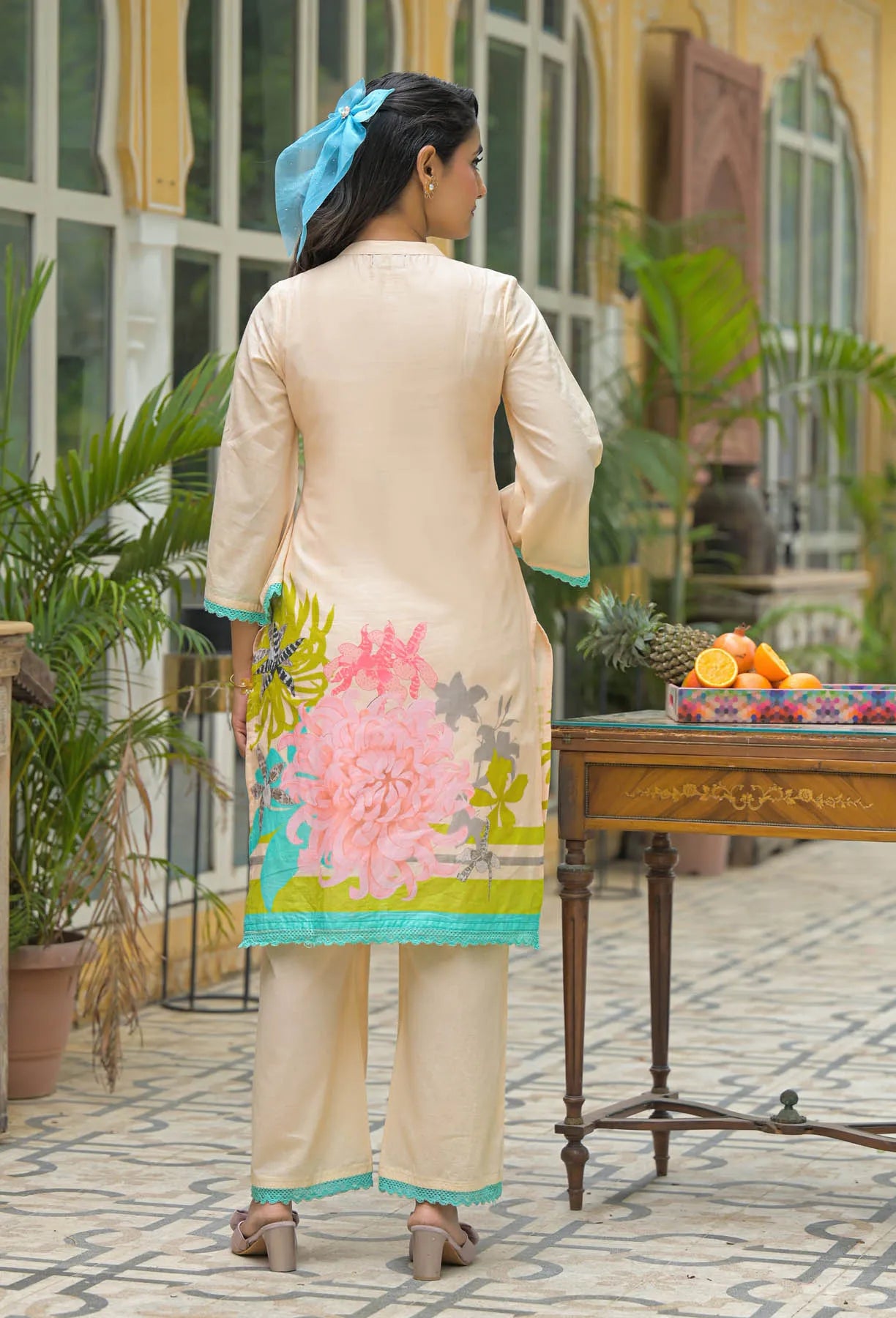 Woman in a floral dress standing near a table with fruits, outdoors.