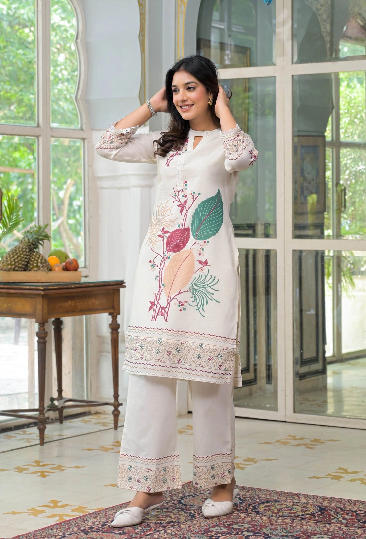 Woman wearing a white embroidered outfit in a bright room with large windows.