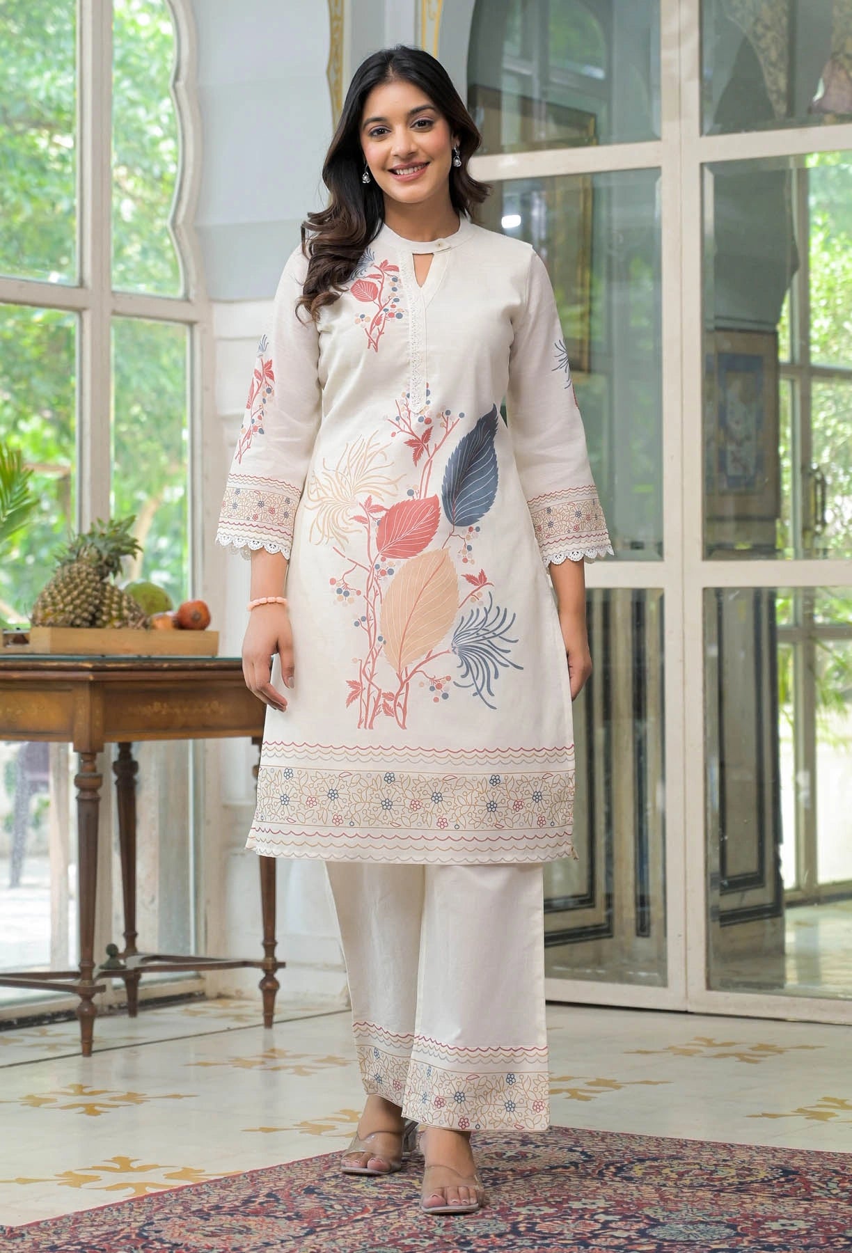 Woman wearing a white embroidered outfit in a room with large windows.