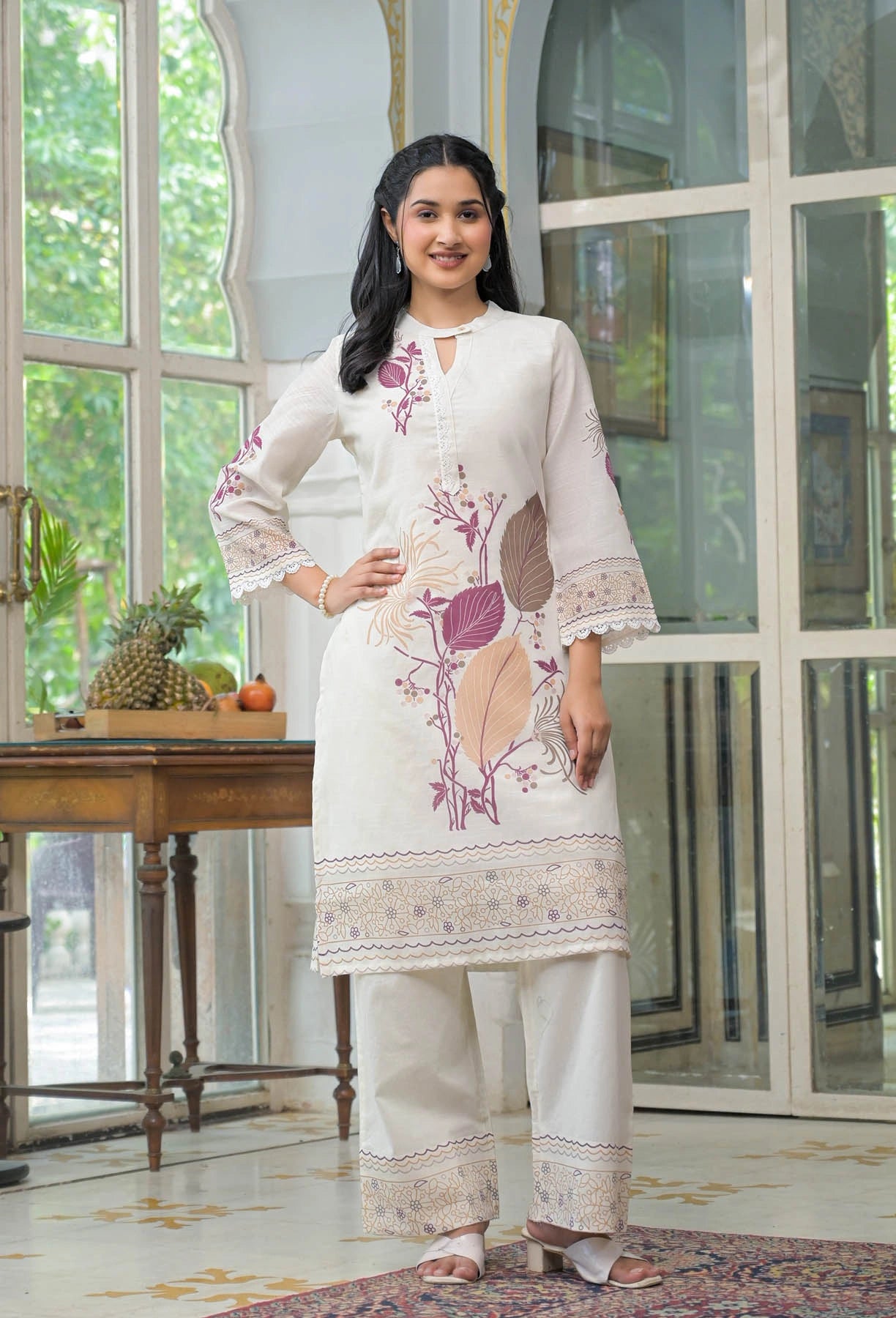 Woman wearing a white embroidered outfit standing in a room with large windows.