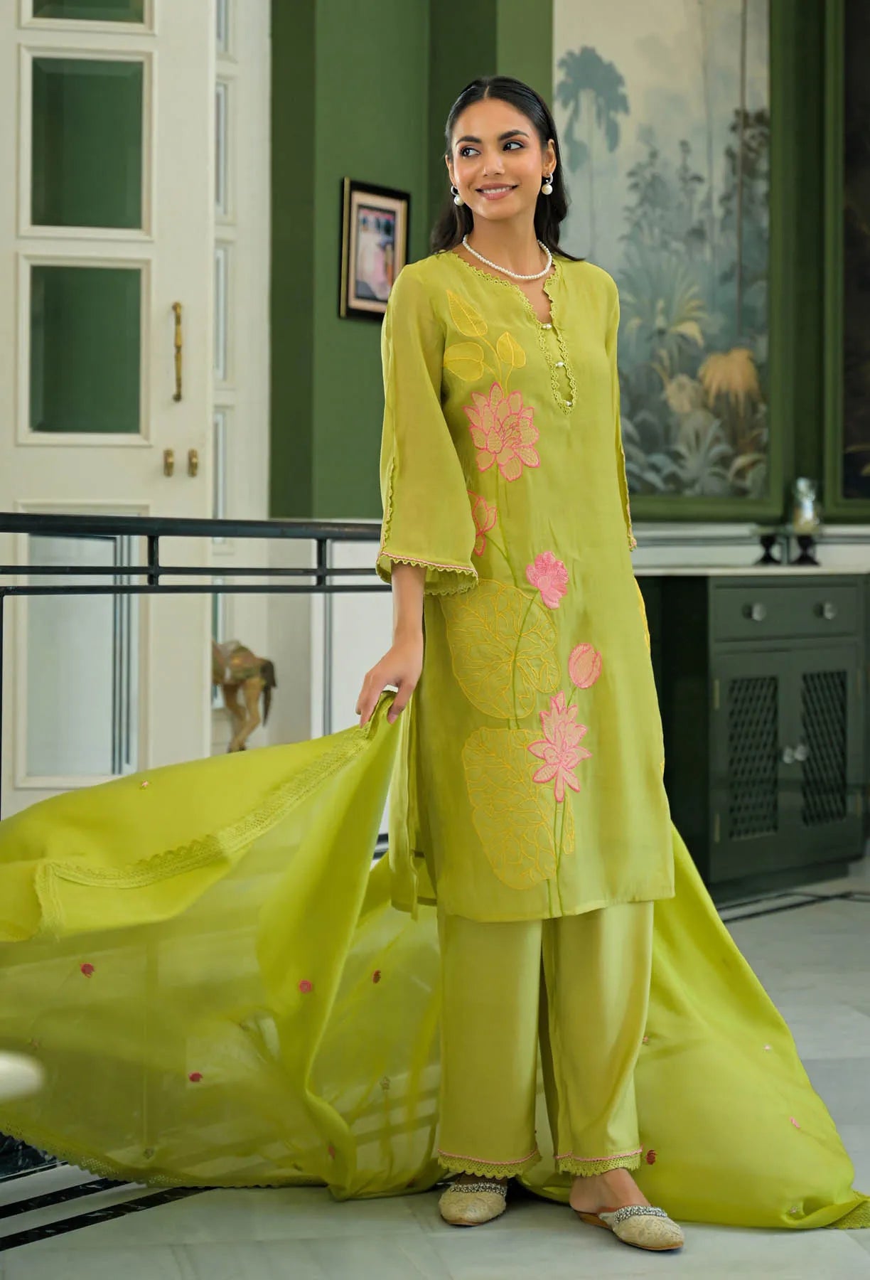 Woman in a light green traditional outfit with floral patterns indoors.