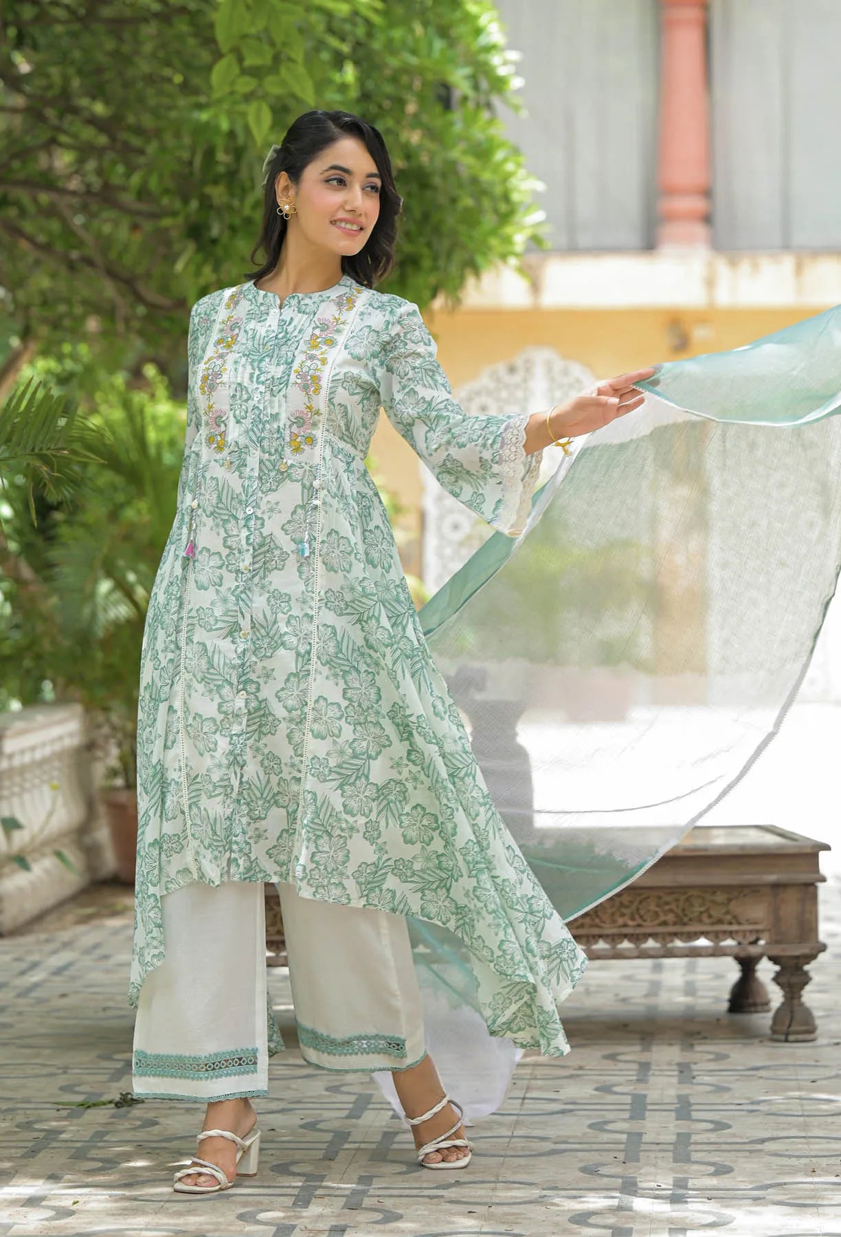 Woman in a light green floral dress holding a dupatta in an outdoor setting.