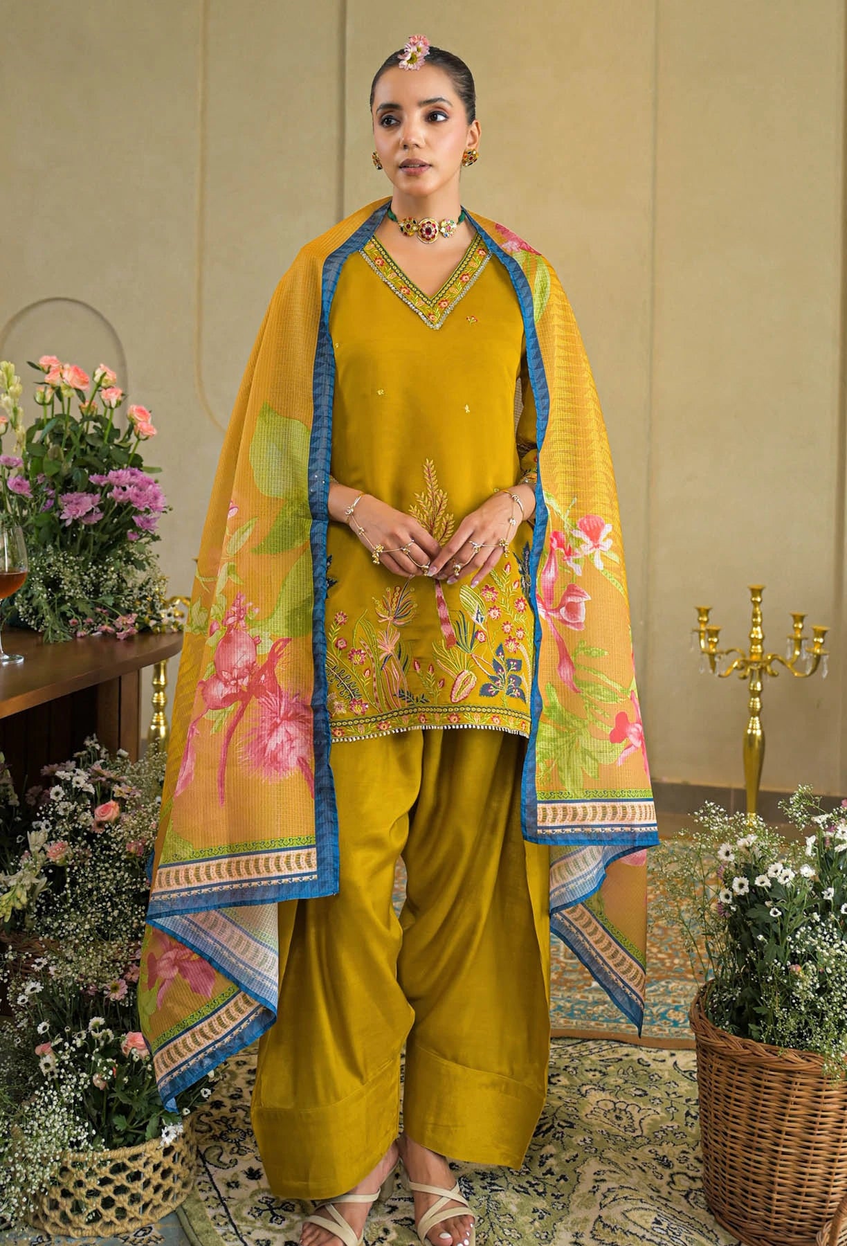 Woman in a yellow traditional outfit with floral patterns in an elegant room.