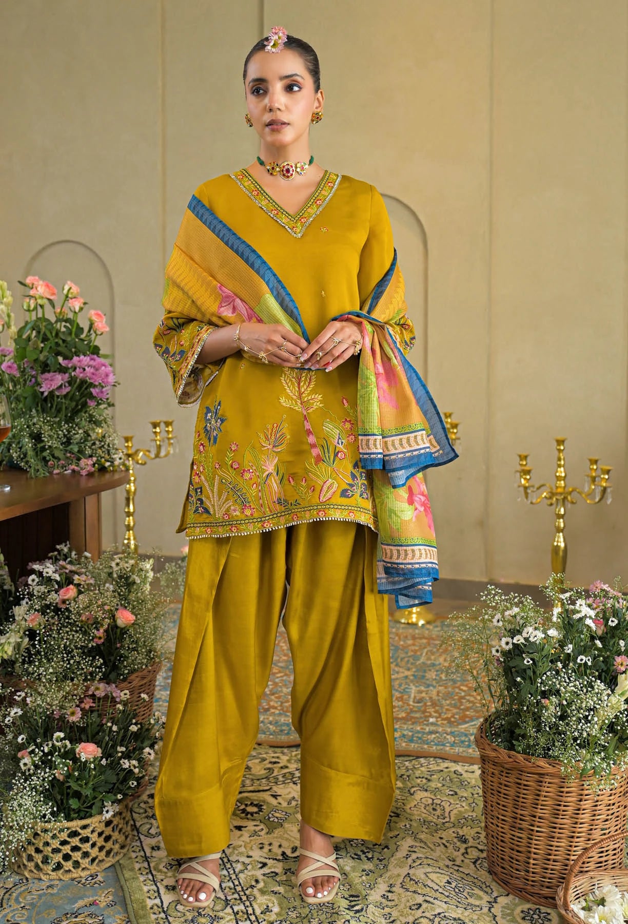 Woman in a traditional mustard yellow outfit with floral patterns in an elegant room.