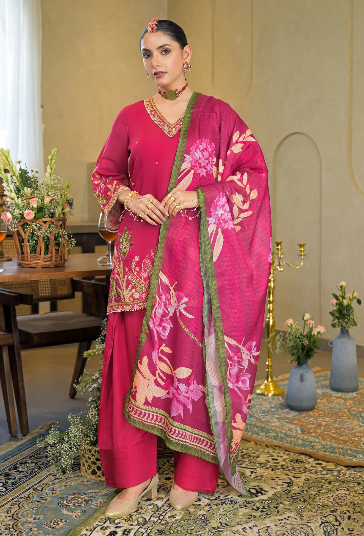 Woman in a pink traditional outfit with floral patterns in an elegant room.