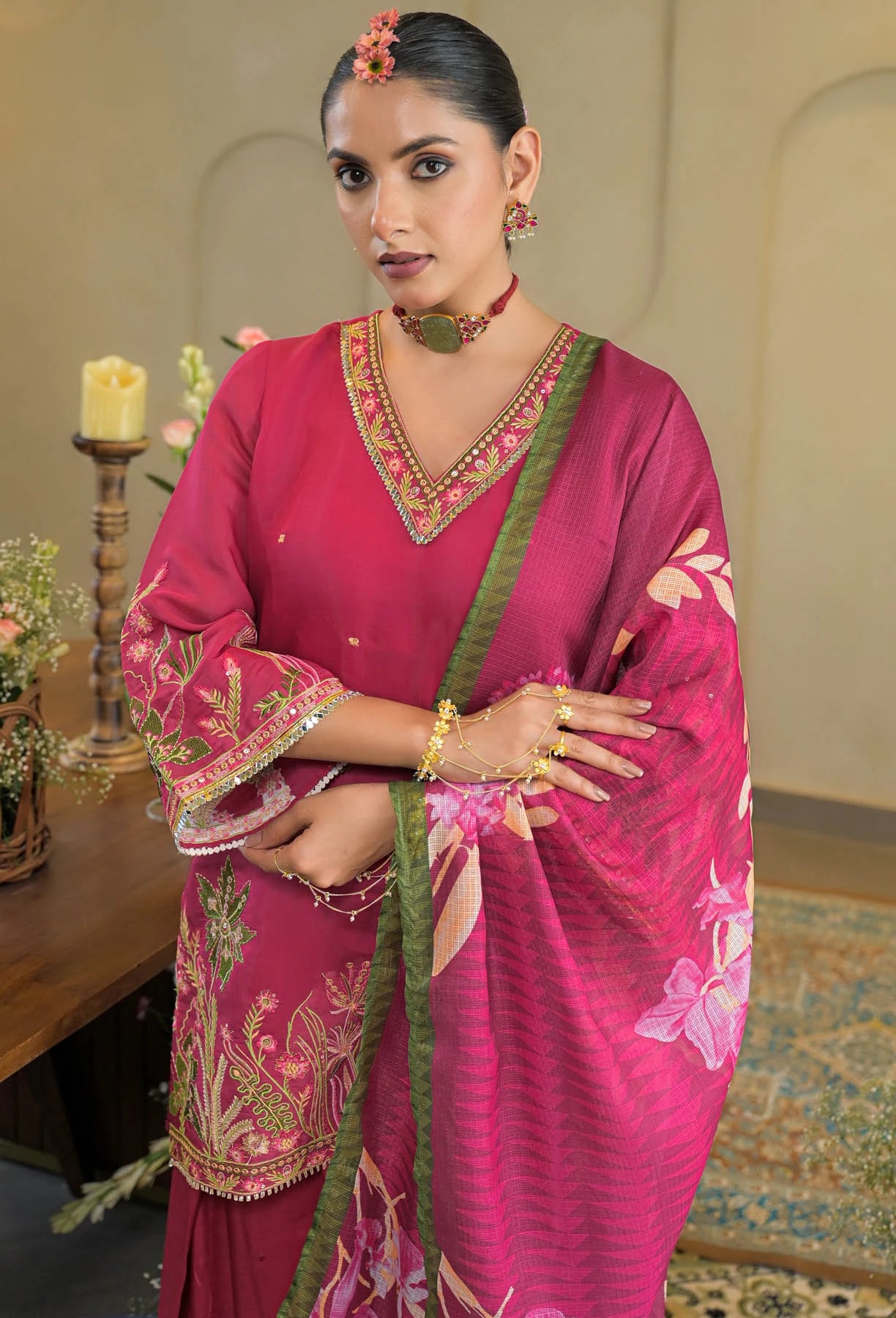 Woman in a pink traditional outfit with floral patterns, standing indoors.