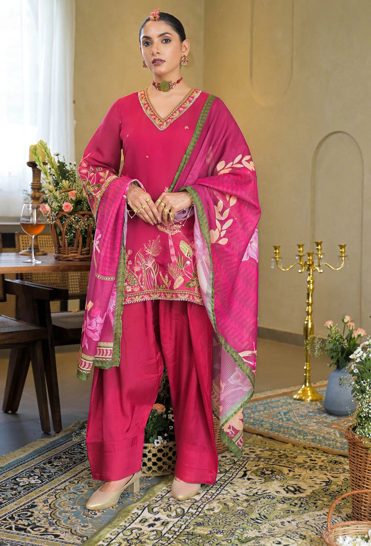 Woman in a traditional pink outfit with intricate designs in a decorated room.