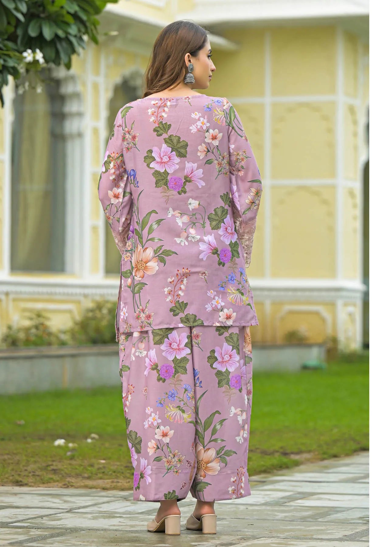 Woman wearing a pink floral outfit standing in front of a yellow building.