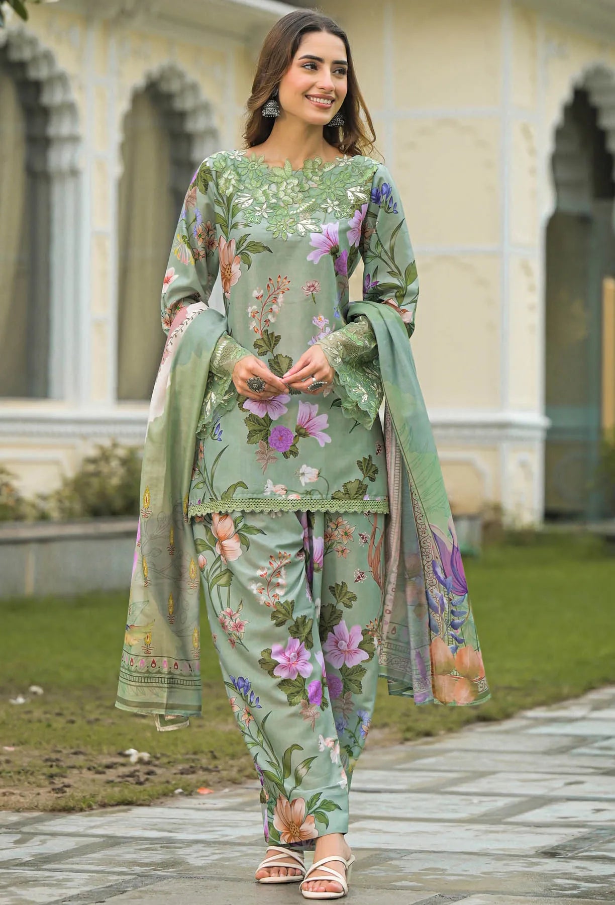Woman wearing a green floral traditional outfit standing in front of a building with arches.