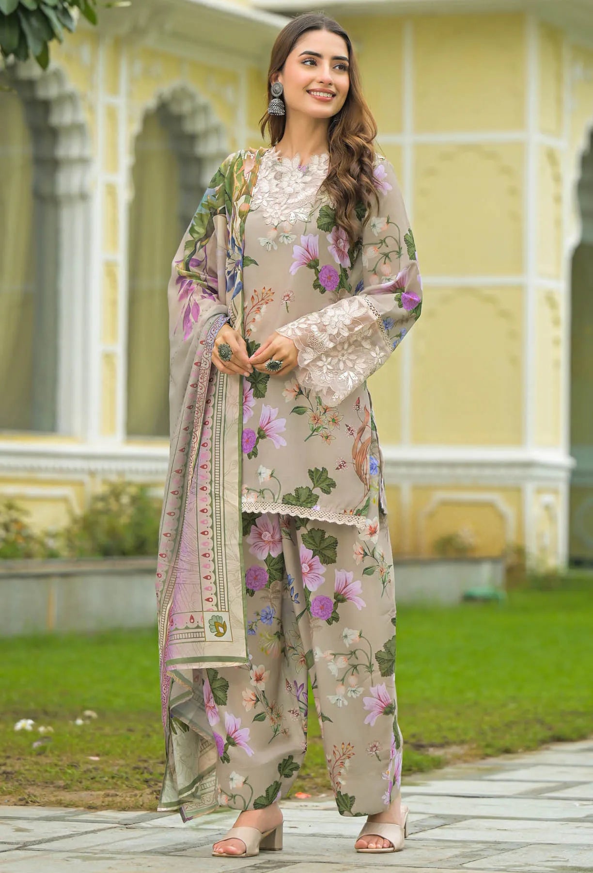 Woman in a floral outfit standing in front of a yellow building with greenery.
