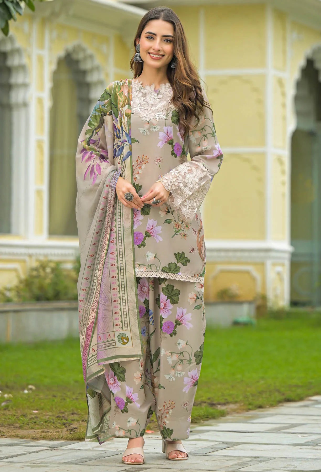 Woman in a floral outfit standing outdoors with a decorative background