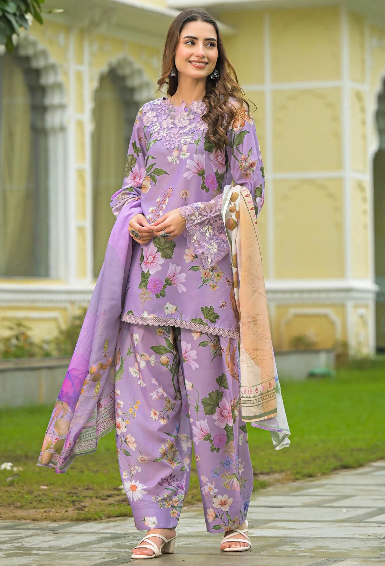 Woman in a purple floral outfit standing in front of a yellow building.