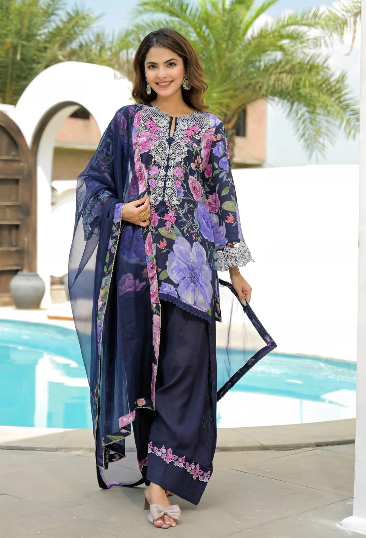 Woman in a floral dress standing by a pool with palm trees in the background