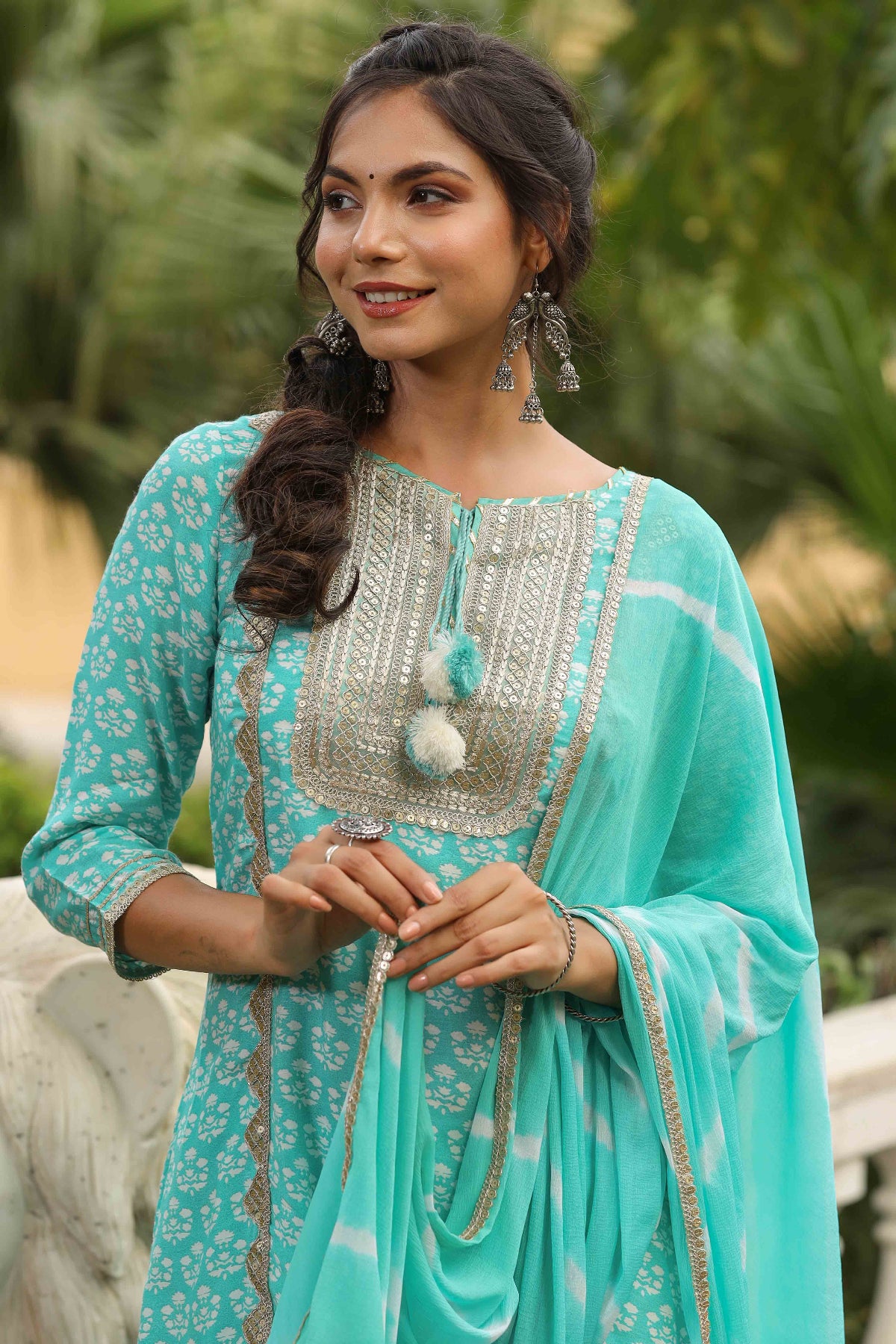 Woman wearing a turquoise traditional outfit with silver embellishments outdoors.