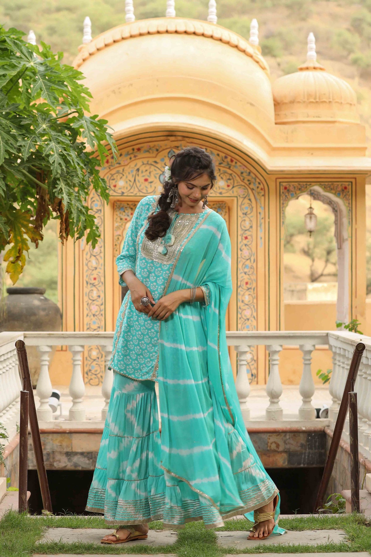Woman in a turquoise traditional outfit standing in front of a decorative building.