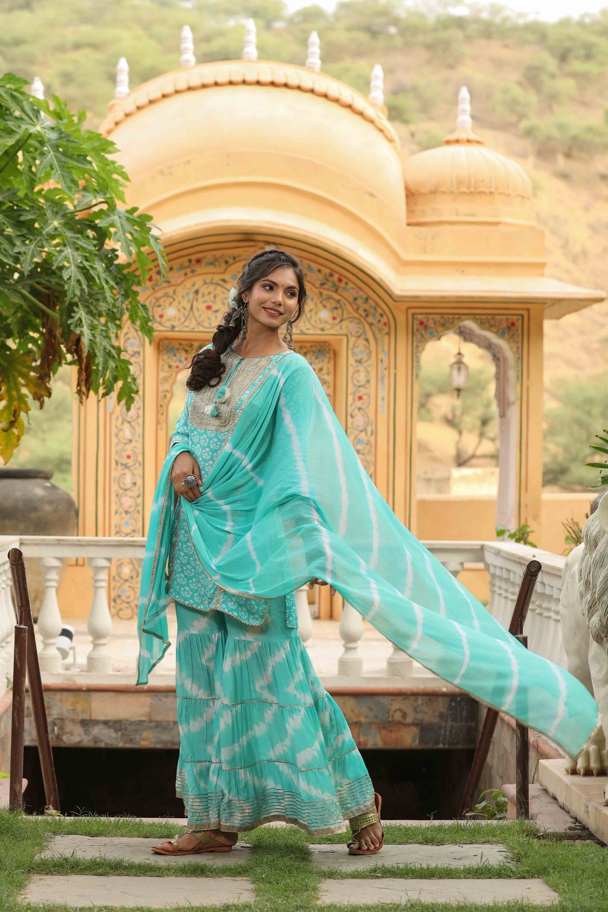 Woman in a teal traditional outfit standing in front of a golden architectural structure.