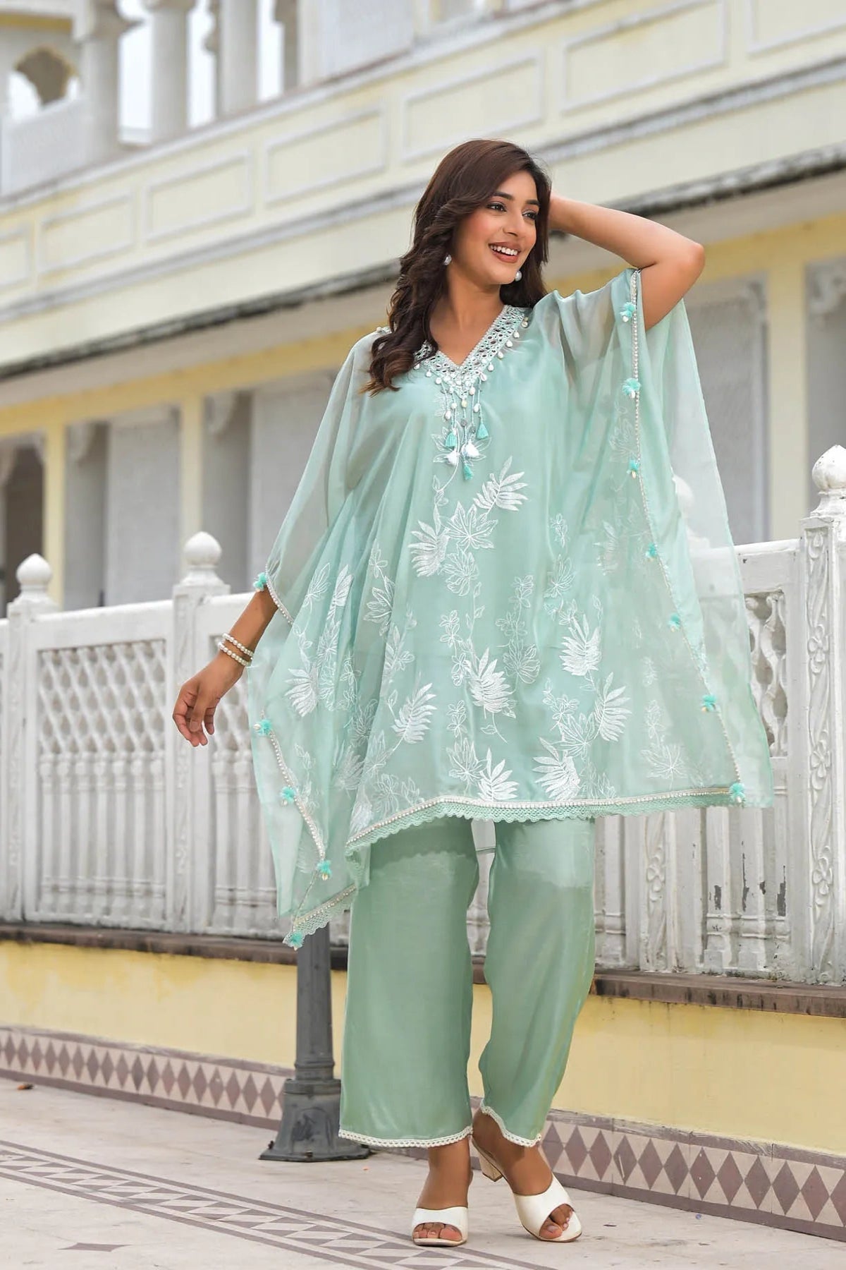 Woman in a light green traditional outfit standing outdoors with a building in the background