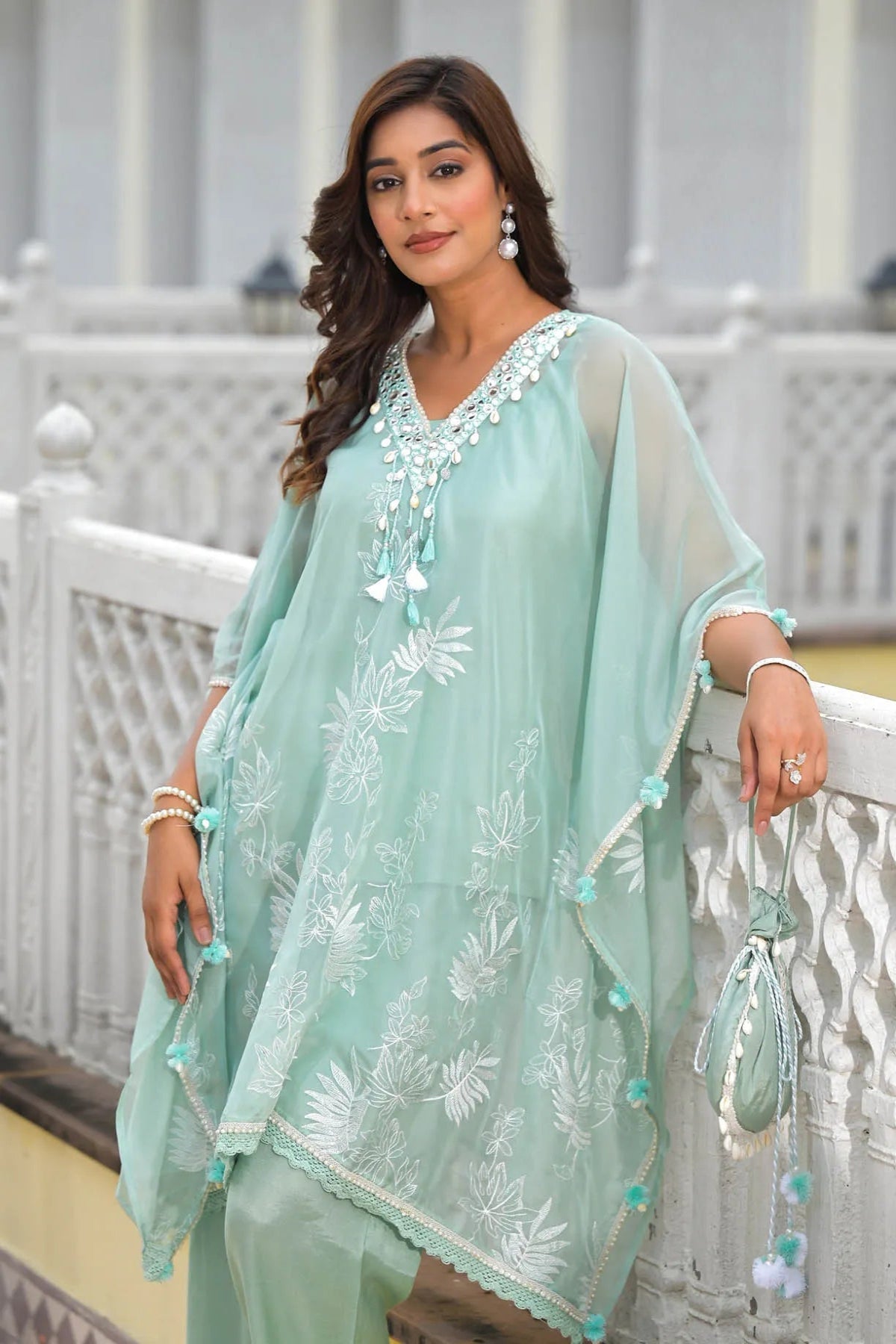 Woman wearing a light green traditional outfit with white patterns, standing on a white railing.