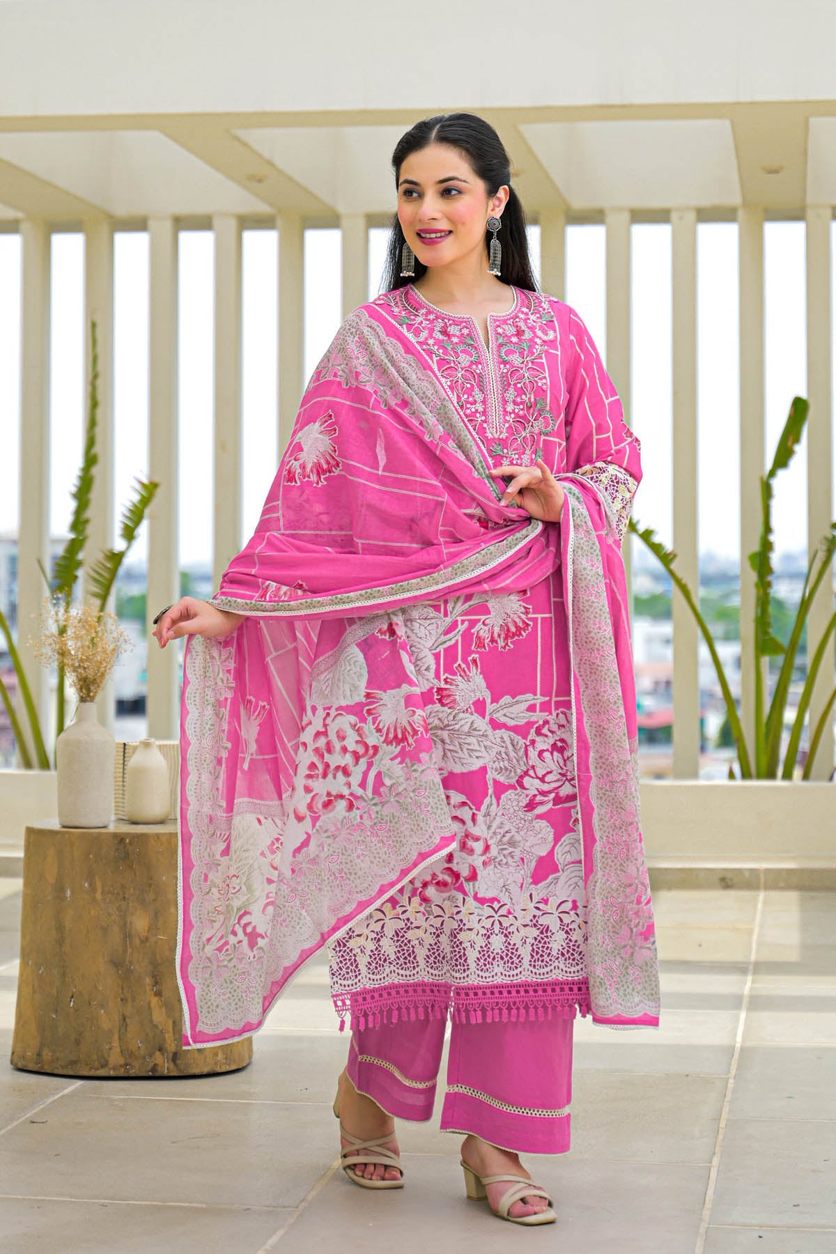 Woman in a pink traditional outfit with white patterns standing indoors.