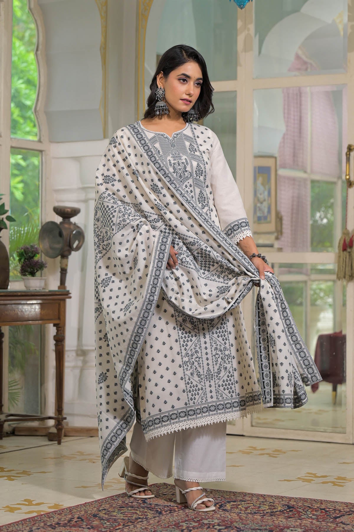 Woman in a white and blue traditional outfit standing in a decorated room.