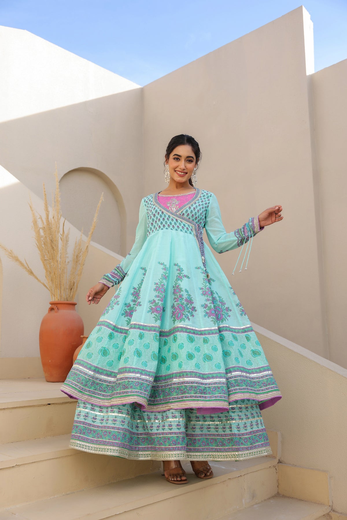 Woman in a light blue traditional outfit standing in front of a white architectural structure.