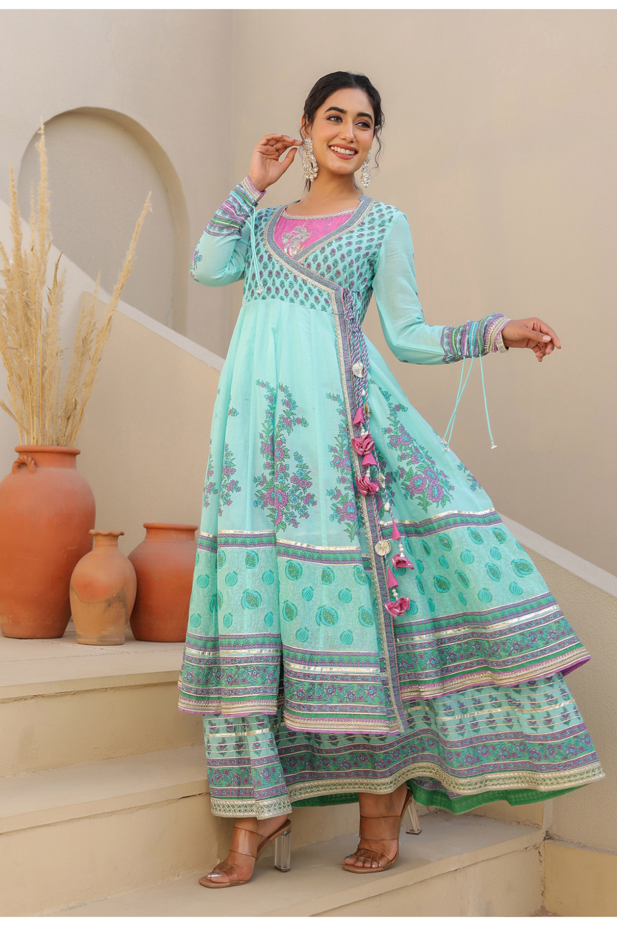 Woman in a traditional outfit standing on steps with decorative vases in the background
