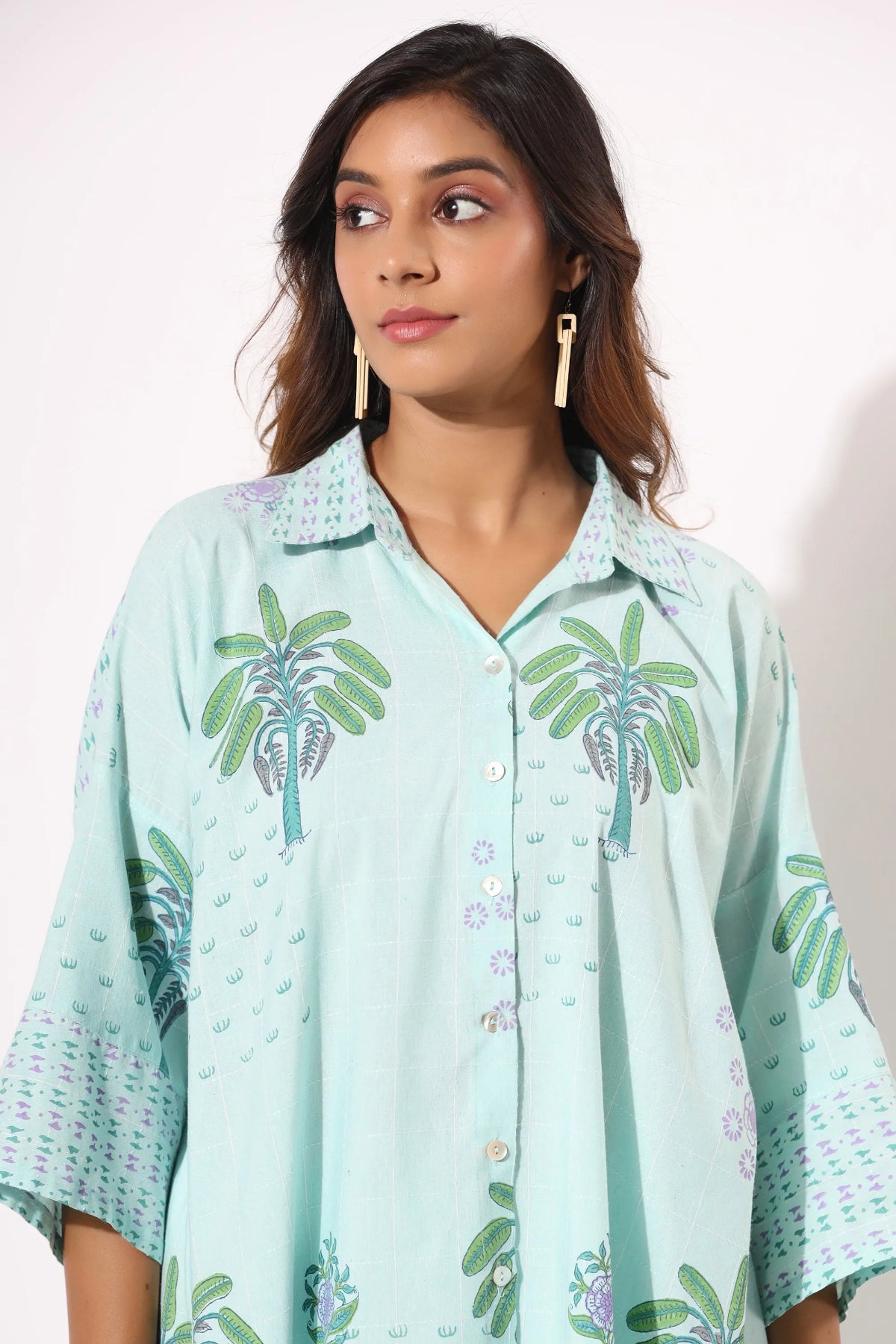 Woman wearing a light blue shirt with palm tree patterns on a white background
