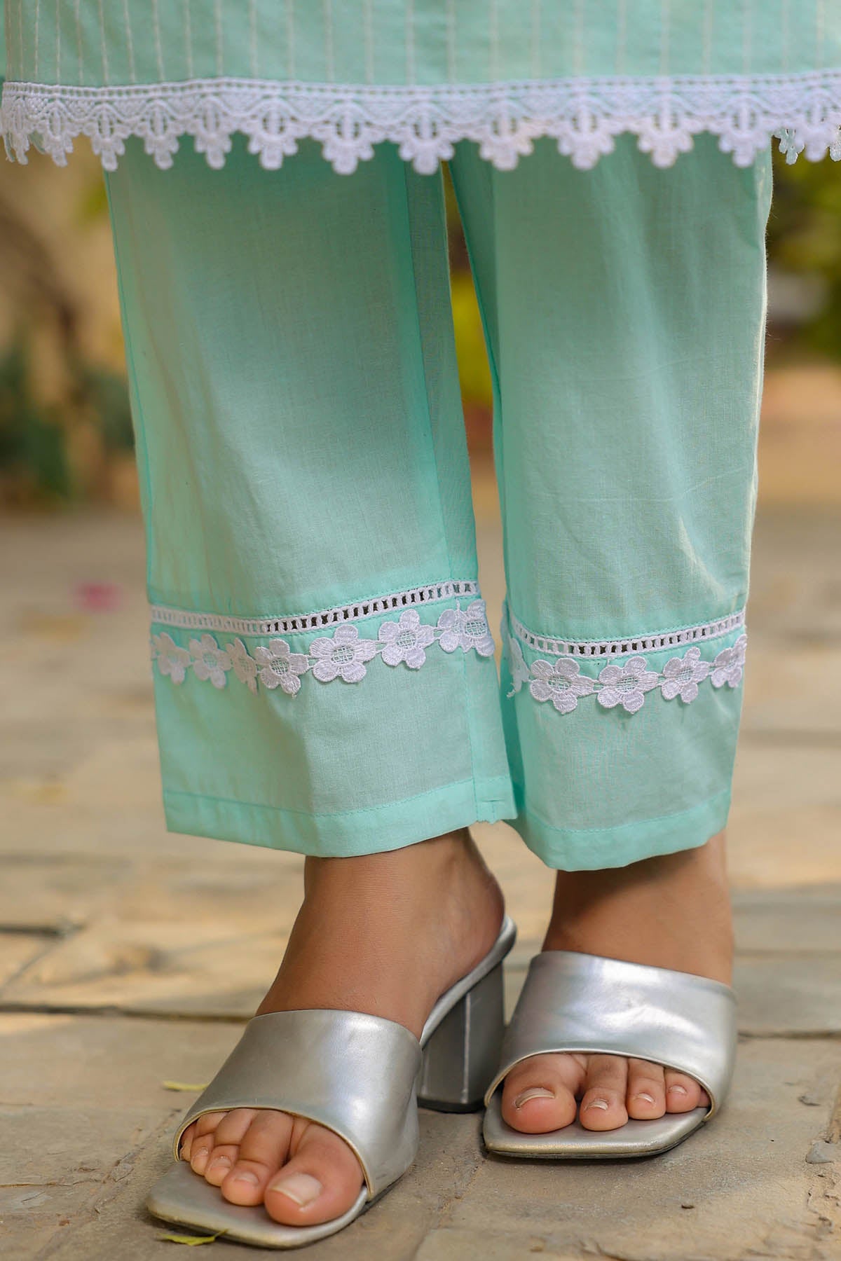 Teal pants with lace details worn by a person, standing on a wooden floor.