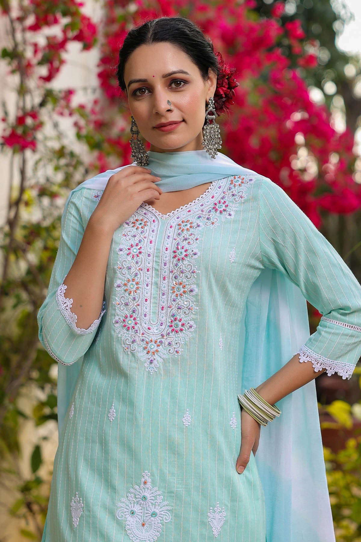 Woman wearing a light blue embroidered traditional outfit with a floral background