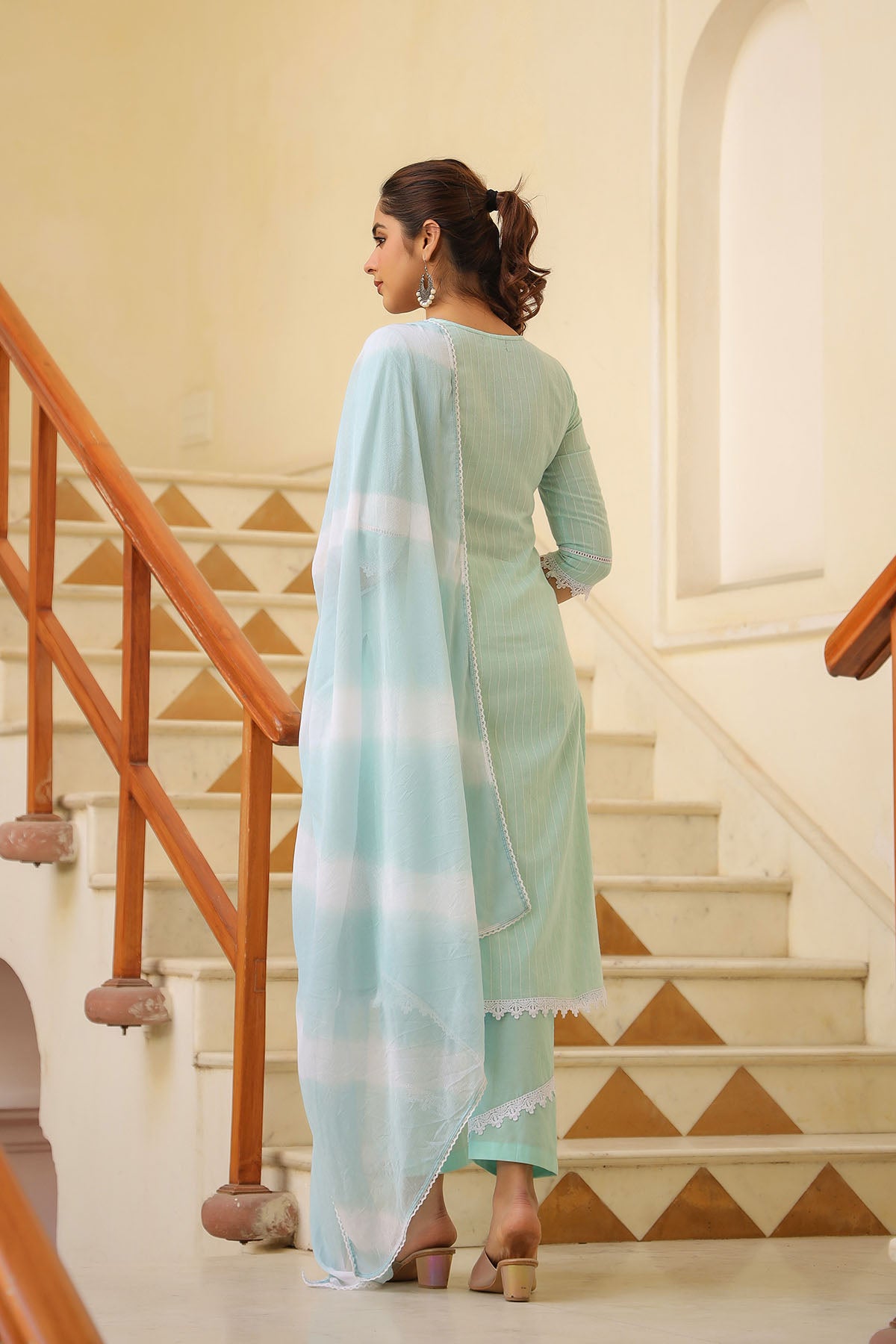 Woman in a light green outfit with a matching dupatta standing on a staircase.
