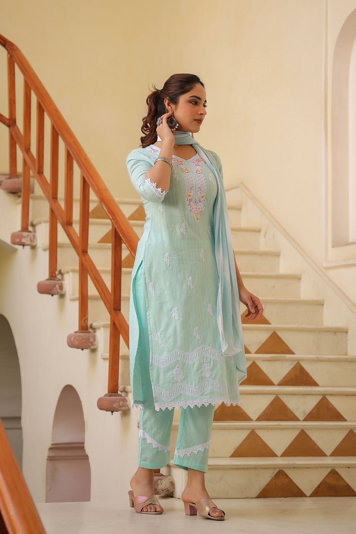 Woman in a light green traditional outfit standing on a staircase with wooden railings.