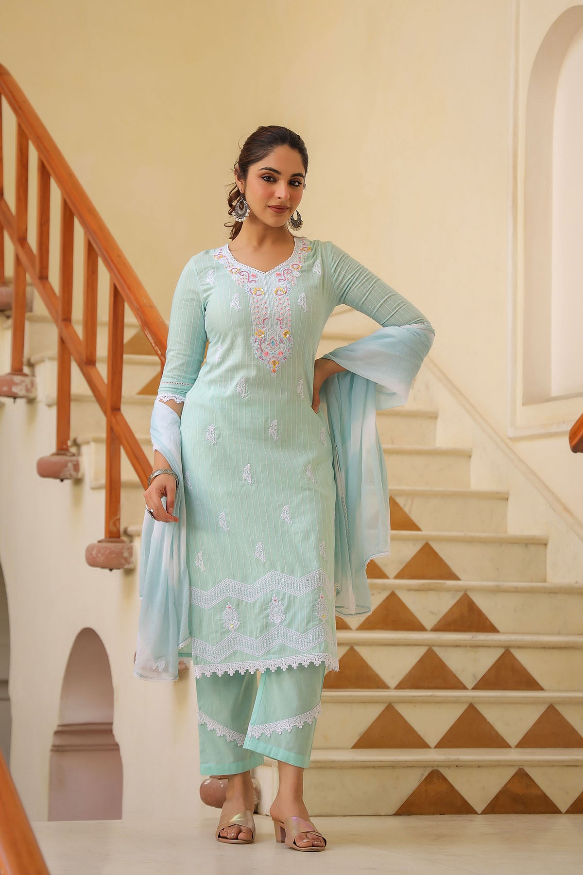 Woman in a light blue traditional outfit standing on a staircase.